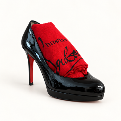 Christian Louboutin black patent pump with red dust bag on off white background